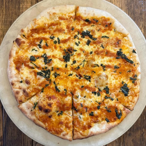 A freshly baked, sliced cheese pizza with basil on a round wooden board.