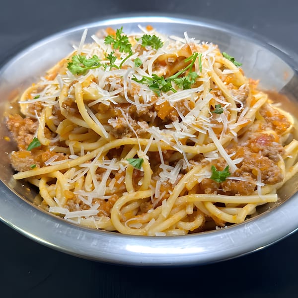 Close-up of spaghetti bolognese in a metal bowl, topped with grated cheese and fresh parsley.
