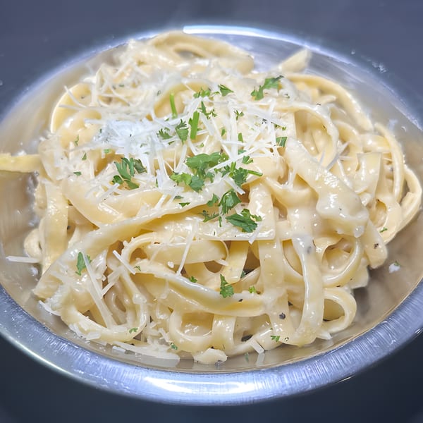 Creamy fettuccine alfredo with grated parmesan cheese and fresh parsley in a metal bowl.