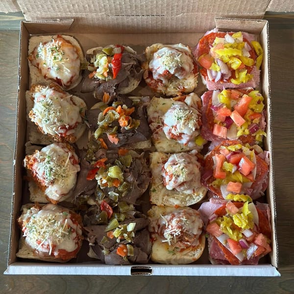 A catering box filled with various Italian sliders, including meatball, Italian beef, and cold cut options.